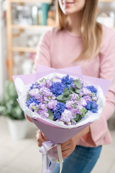 Μπουκέτα με μπλε υάκινθοι και Μαθιόλα λιλά χρώμα στο χέρι γυναίκα. Άνοιξη λουλούδια από ολλανδική κηπουρό. Έννοια του ένα ανθοπωλείο σε ένα ανθοπωλείο. Ταπετσαρία. - Φωτογραφία, εικόνα