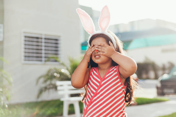 Cute little girl with bunny ears and basket of Easter eggs in the garden. Easter egg hunt - Valokuva, kuva