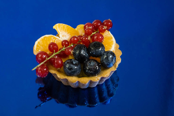 Cupcake-friss bio gyümölcs, narancs, áfonya, ribizli, side view fénykép, tükör kék háttér - Fotó, kép