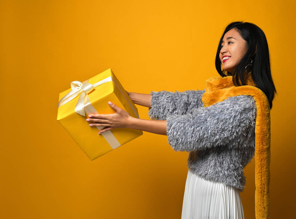 Portrait of a smiling pretty girl holding gift box isolated over yellow background - Fotografie, Obrázek