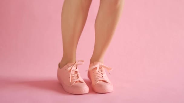 Close up of slim female legs dancing in sneakers on coral background - Imágenes, Vídeo