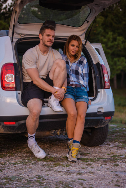 Nuori pari istuu maastoauton takana ja nauttii
 - Valokuva, kuva