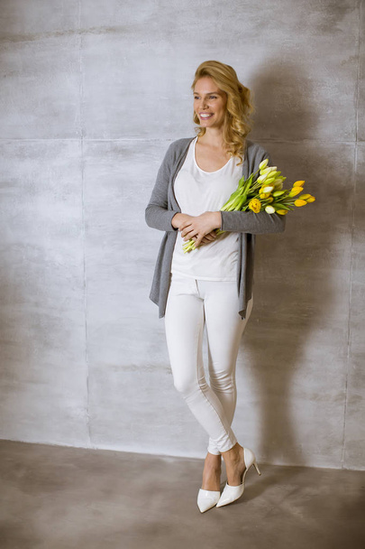 Young woman with a bouquet of yellow tulips standing by the wall - Foto, imagen