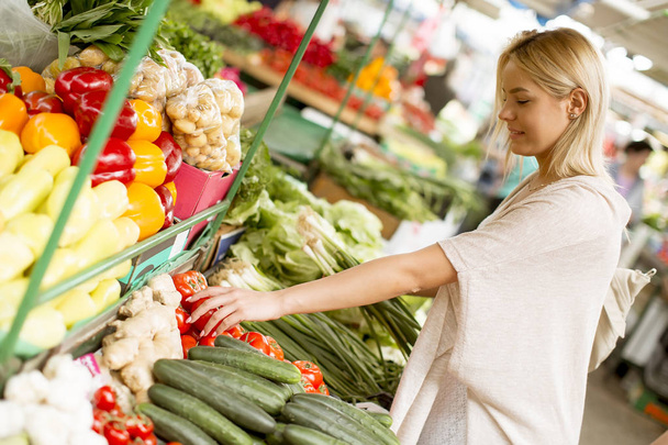 Вид на красиву молоду жінку, яка купує овочі на ринку
 - Фото, зображення