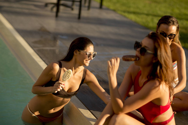 Muotokuva kolmesta nuoresta houkuttelevasta naisystävästä, jotka syövät jäätelöä pyyhkäisemällä uima-altaalla kesäpäivänä
 - Valokuva, kuva