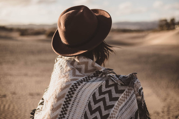young woman from backwards with scarf and hat in the desert at sunset - Fotoğraf, Görsel