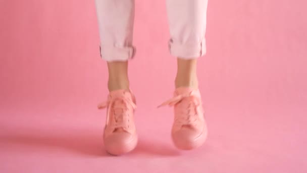 Nahaufnahme schlanker weiblicher Beine, die in Turnschuhen auf korallenfarbenem Hintergrund tanzen - Filmmaterial, Video