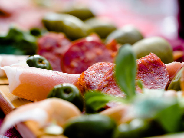 Tapas met salami, ham, kaas en zwarte olijven, groene olijven op een licht patroon Schotse tartan servet. Close-up. Een aperitief of een snack in de Spaanse keuken in Spanje. - Foto, afbeelding