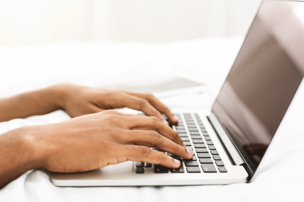 Блогер чорного чоловіка, який друкує на ноутбуці в ліжку
 - Фото, зображення