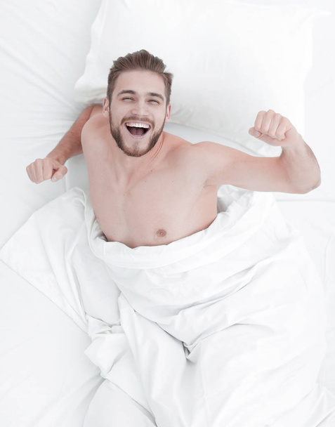 top view. happy man sitting on the comfortable bed - Фото, изображение