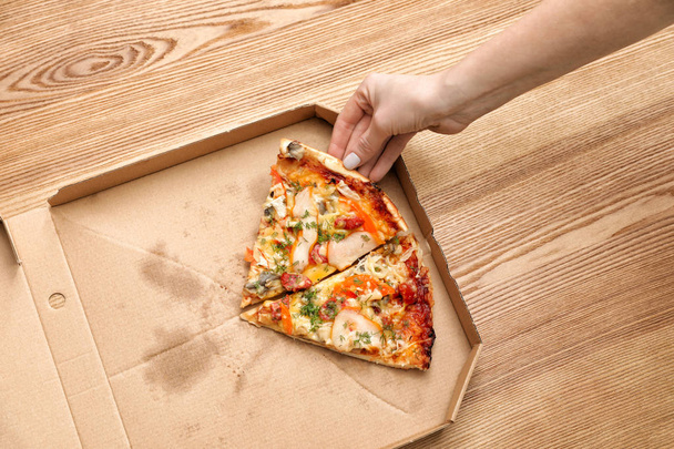 Woman taking pizza piece out of box on wooden table, top view - Photo, image