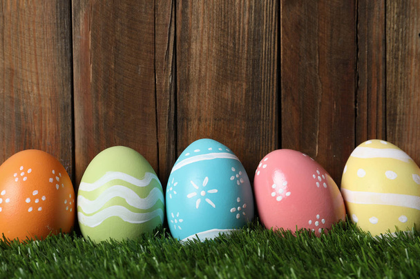 Colorful painted Easter eggs on green grass against wooden background, space for text - Фото, зображення