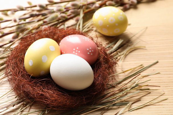 Sisal nest with painted Easter eggs on wooden table. Space for text - Фото, изображение