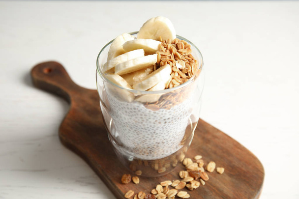 Glass of tasty chia seed pudding with banana and granola served on table - Foto, imagen