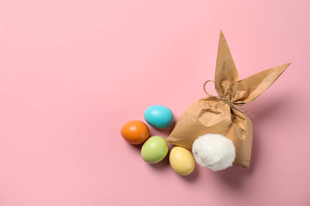 Flat lay composition of Easter bunny gift bag and dyed eggs on color background. Space for text - Foto, afbeelding