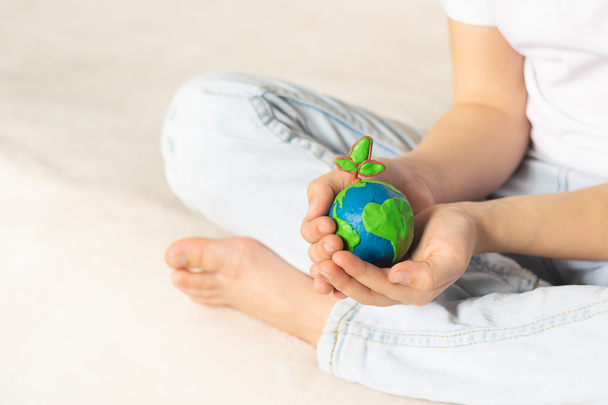 Un pequeño globo con árboles en las manos de un niño. Diseño del planeta hecho de plastilina en palmas de niños. Concepto
 - Foto, imagen