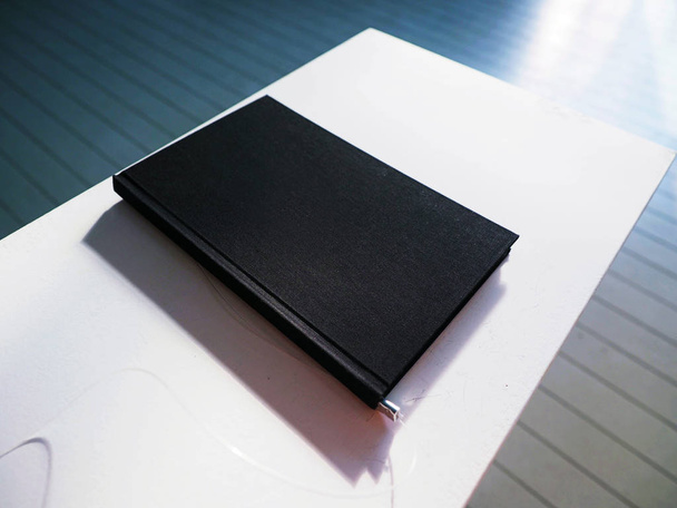 Черный дневник на белом столе в современной пустой офисной комнате, макет, макет
 - Фото, изображение