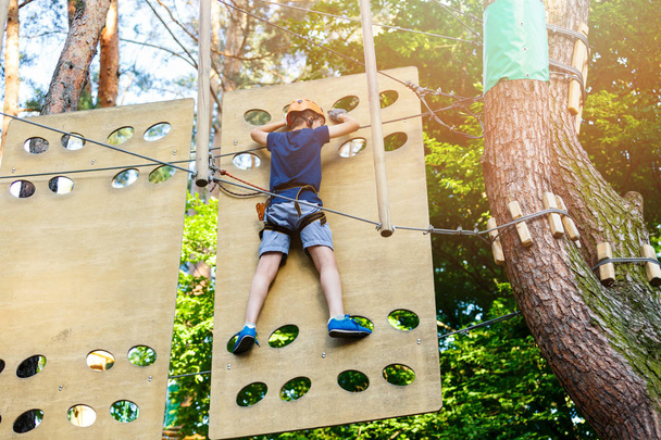Cute young boy in helmet with climbing equipment in the rope amusement park. Summer camp, holidays concept. Active lifestyle  - Photo, Image