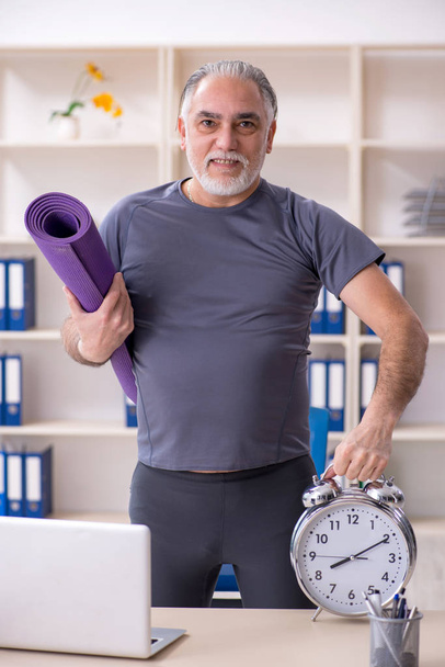 White bearded old man employee doing exercises in the office  - Photo, Image