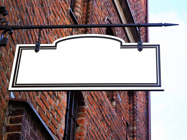 Signboard side view of empty white mock up signage in black frame with old city red brick wall background display exterior. Medieval, middle age style with artistic metal blacksmithing decoration - Photo, Image