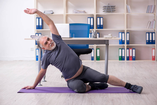 Белый бородатый старик работник делает упражнения в офисе
  - Фото, изображение