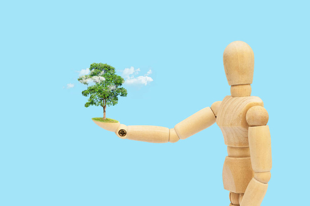 Pojęcie ekologii: Drewniana figura manekin trzymając w ręku drzewo zielony i biały chmura. - Zdjęcie, obraz