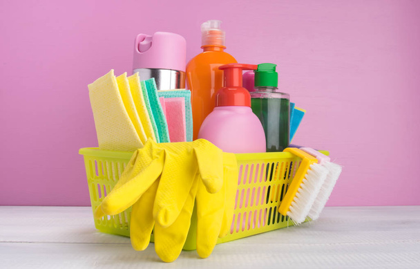 in a yellow basket, on a pink background, a set of items for cleaning, rags, sponges, brushes, liquids for disinfection - Фото, зображення
