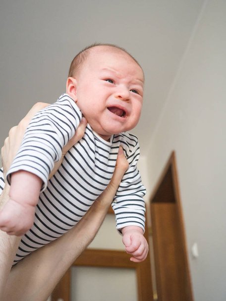 叫ぶ赤ちゃんの男の子を泣く彼の親が家で泣くのをやめるために空中に抱かれている混合レース - 写真・画像