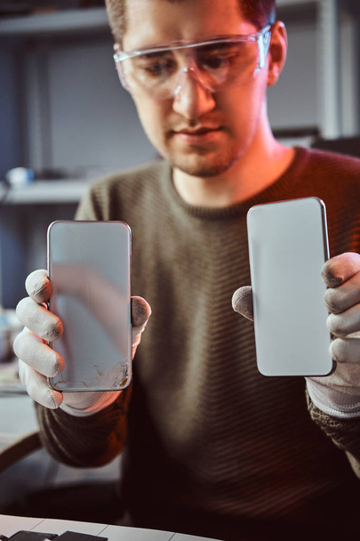 Technician holds two identical smartphones for comparison, in one hand broken and in another new - Foto, immagini