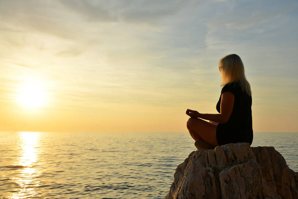 vrouw beoefenen van yoga door de zee bij zonsondergang. - Foto, afbeelding