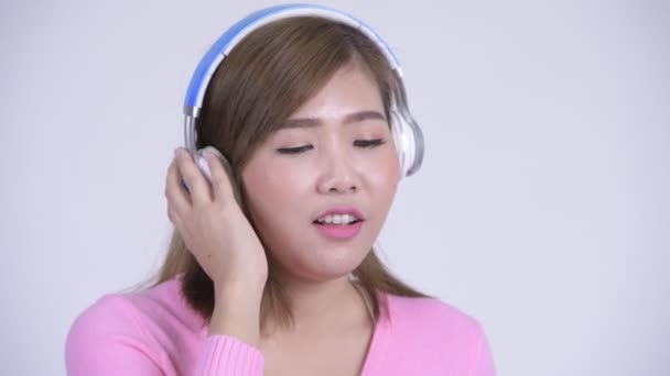 Face of young happy Asian woman thinking while listening to music - Πλάνα, βίντεο