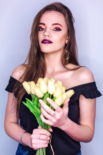 Beauty portrait of a woman with bright colorful make-up and bouquet of yellow tulips - 写真・画像