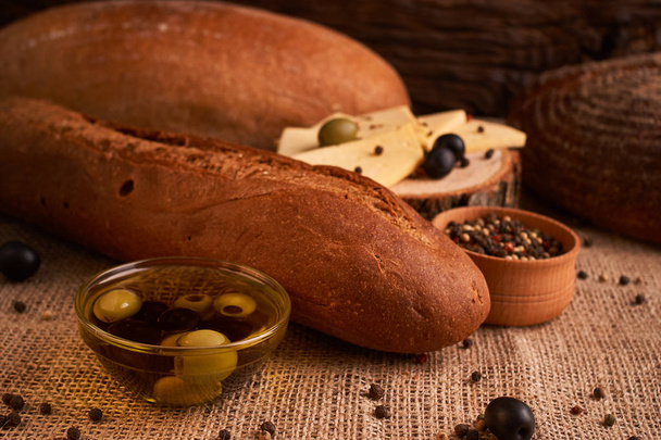 baguette de pan fresco con aceite de oliva, aceitunas. queso y romero sobre fondo de madera. Desayuno teasty
 - Foto, imagen