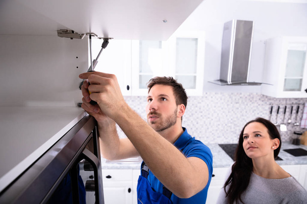 Woman Looking At Male Handyman Installing Cabinet Door In The Kitchen - Фото, зображення