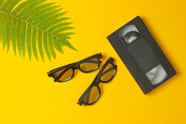 3D glasses, video cassette, fern leaf on a yellow background. Top view, minimalis - Photo, Image
