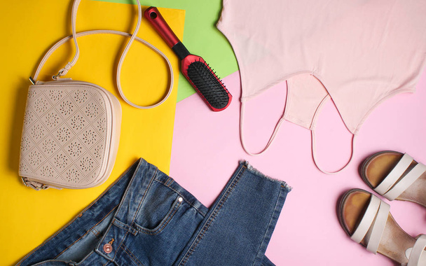 Acessórios femininos e roupas em um fundo pastel colorido. Jeans, sandálias, t-shirt, saco, pente. Vista superior, flat la
 - Foto, Imagem