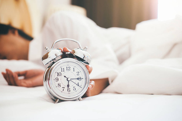 Роздратована молода жінка відкладає будильник вранці з м'яким ранковим світлом. Розслаблююча концепція
. - Фото, зображення