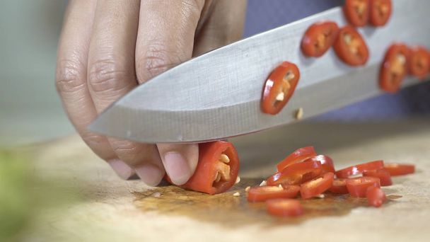 Krojenie chili z nóż kuchenny na płycie, z bliska. - Zdjęcie, obraz
