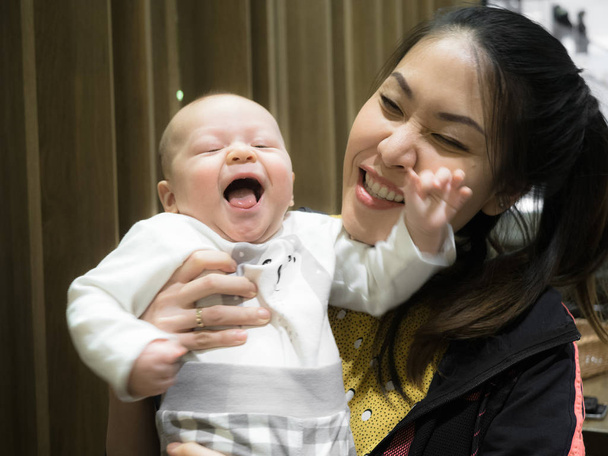 Счастливая азиатская молодая мать, сидящая в ресторане, разговаривающая, счастливый ребенок, смешанная расовая семья, наполовину азиатская наполовину европейская. Ребенок, молодая семья
 - Фото, изображение