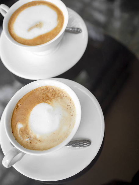 Две белые керамические чашки кофе на стеклянном столе
 - Фото, изображение