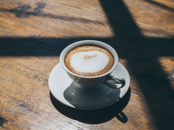 Café caliente en taza redonda de cerámica blanca sobre fondo de mesa de madera
 - Foto, imagen