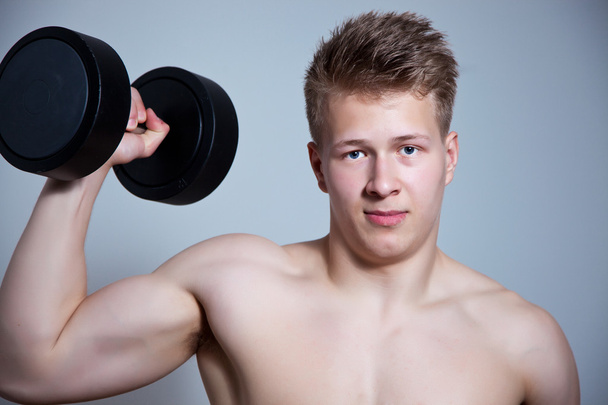 Egy egészséges fiatal srác vállát gyakorolja a súlyzó, egy fehér háttér elölnézete - Fotó, kép