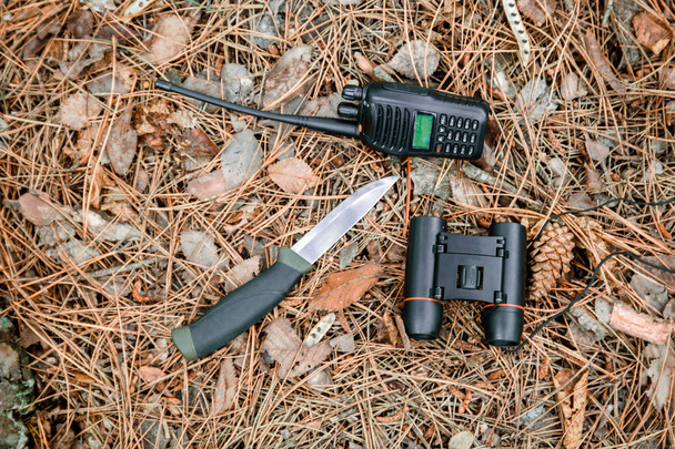 prismáticos, radio set y cuchillo de caza en el suelo cubierto con agujas de pino
 - Foto, imagen