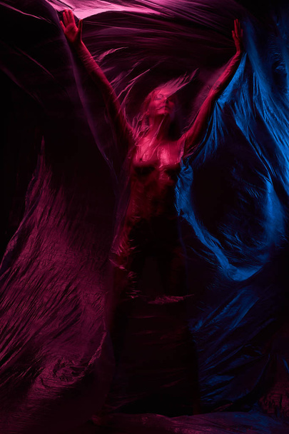 Art nude portrait of woman posing with polyethylene in violet, blue and red lights. Studio shot. - Foto, Imagem