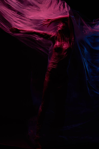 Art nude portrait of woman posing with polyethylene in violet, blue and red lights. Studio shot. - Фото, изображение