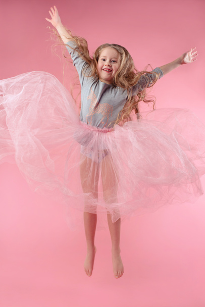 cute funny little girl with long blonde hair jumping on pink background - Photo, Image