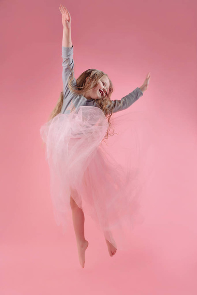 cute funny little girl with long blonde hair jumping on pink background - Фото, изображение