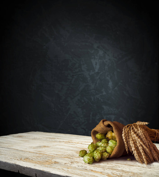 Beer, brewery background. Fresh green hop and wheat with wooden barrel on vintage table. Ingredients for brewing. Retro style. Beer brewing traditions. Copy space for your text - Photo, Image
