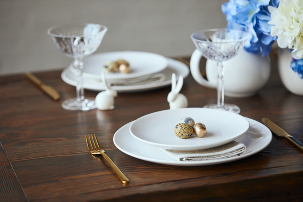 selective focus of quail eggs on white plates, crystal glasses and decorative bunnies on wooden table at home - Foto, Bild