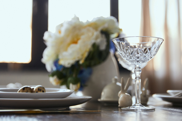 selective focus of crystal glass, bouquet in vase and decorative rabbits on wooden table at home - Photo, Image